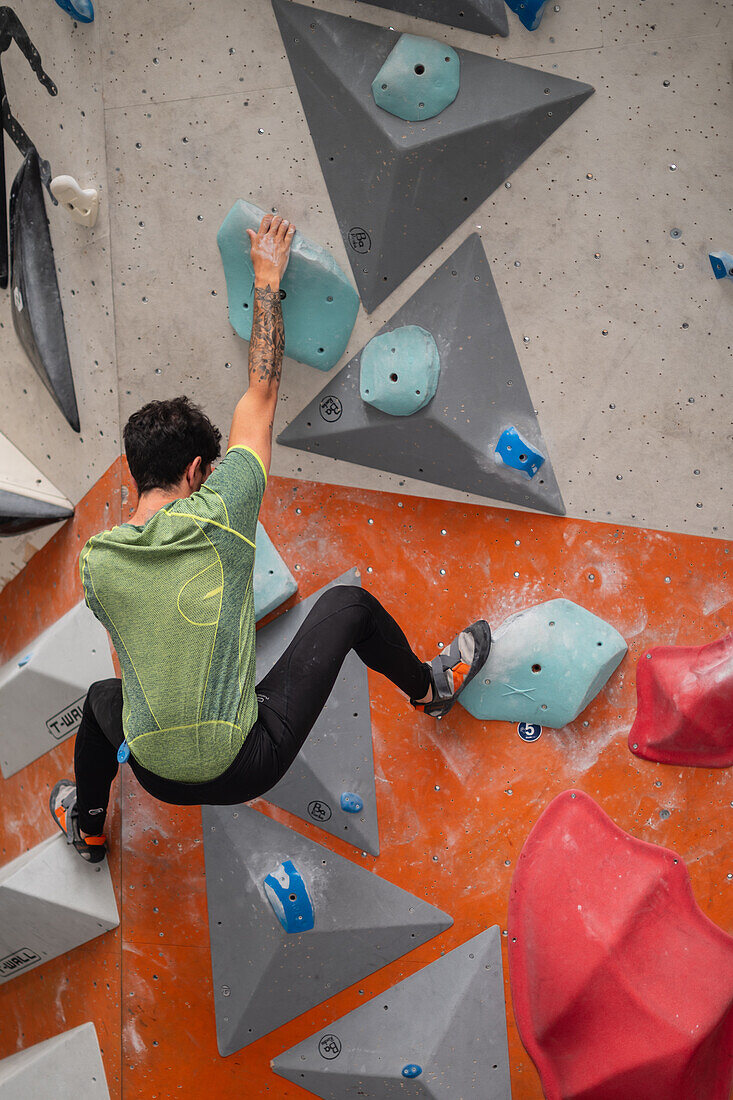 Junger Mann in den Zwanzigern beim Klettern an einer Kletterwand in einer Halle