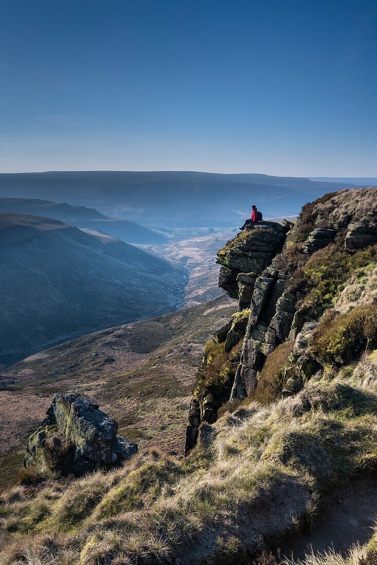 Walker sitting on Laddow Rocks looking out over Crowden Great Brook valley, Peak District National Park, Derbyshire, England, United Kingdom, Europe