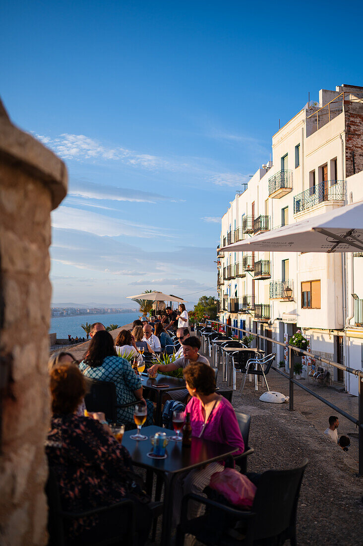 Besucher genießen den Sonnenuntergang von einem Restaurant auf der Stadtmauer der Burg Papa Luna in Peñiscola, Castellon, Valencianische Gemeinschaft, Spanien