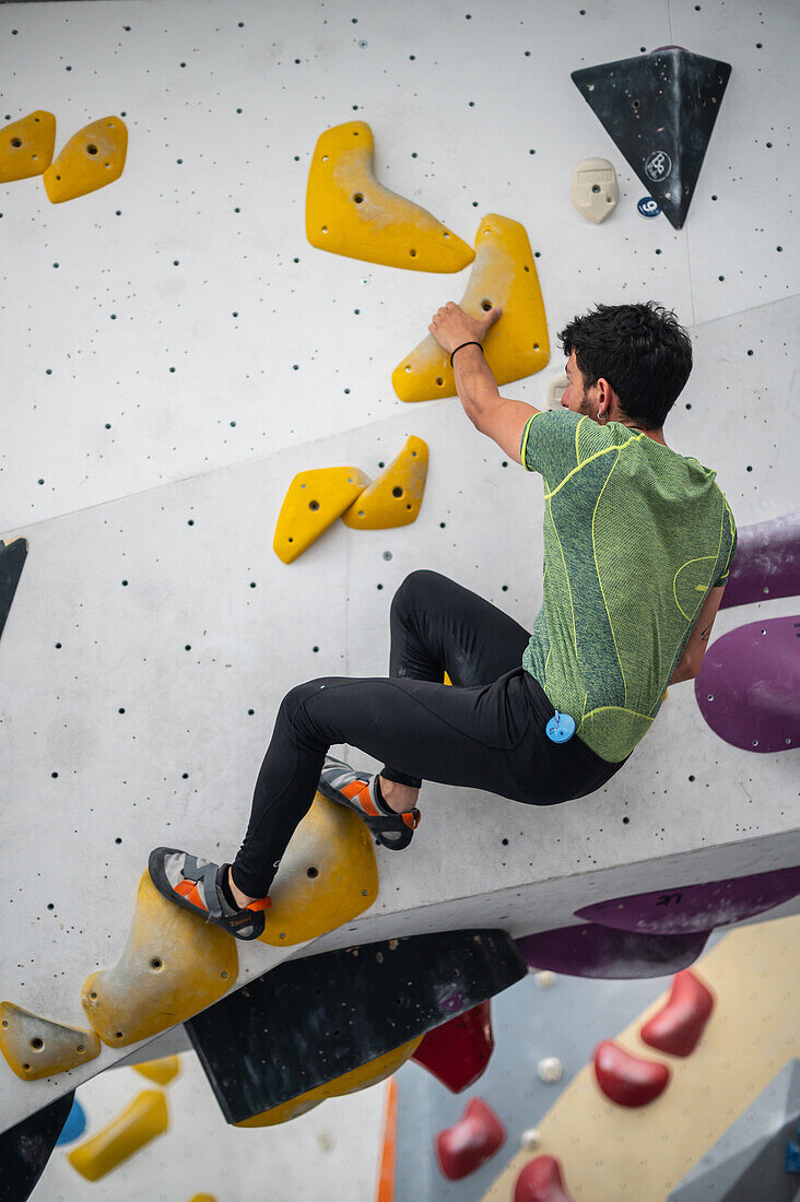 Junger Mann in den Zwanzigern beim Klettern an einer Kletterwand in einer Halle