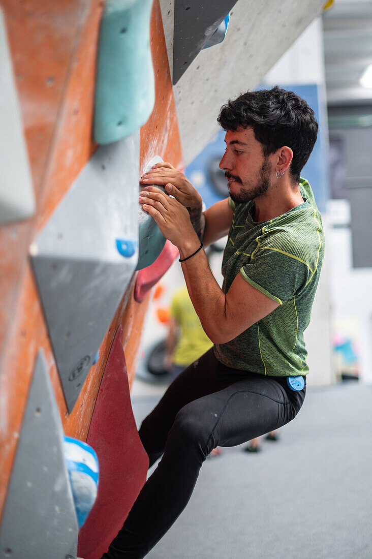 Young man in his twenties climbing on a climbing wall indoors