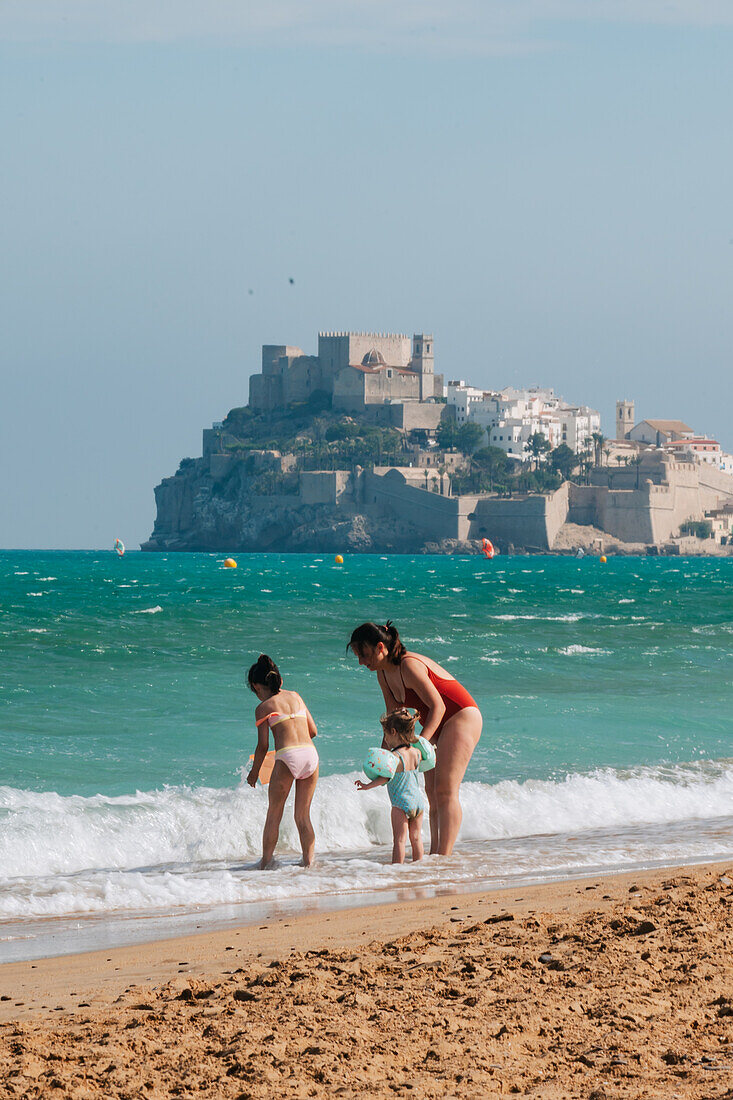 Family on the beach and view of Papa Luna castle in Peñiscola, Castellon, Valencian Community, Spain