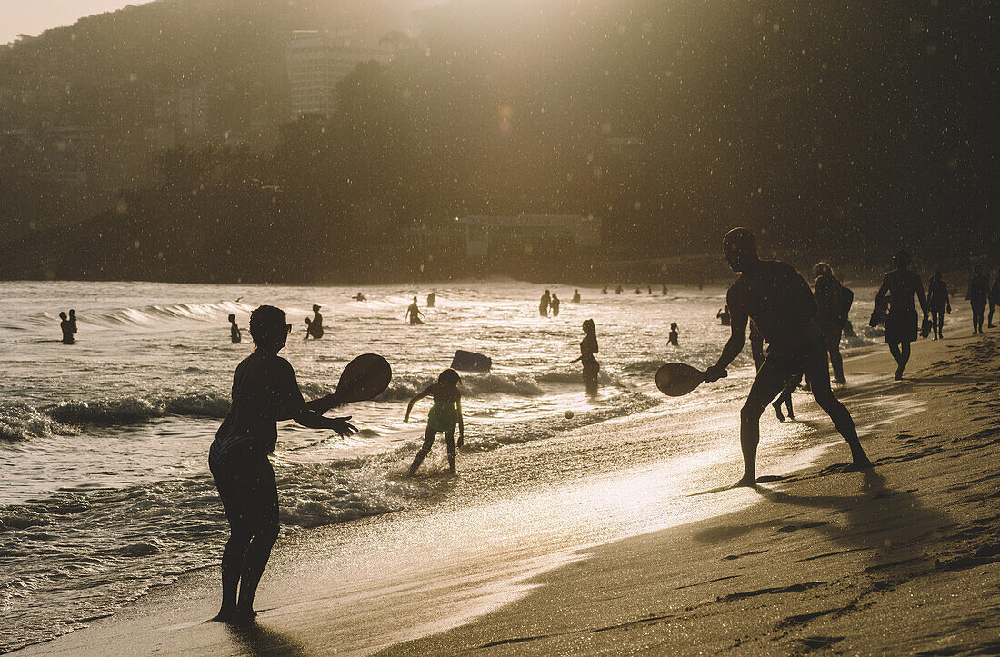 Menschen spielen Racquetball am Strand von Leblon, bei Sonnenuntergang und leichtem Nieselregen, Rio de Janeiro, Brasilien, Südamerika