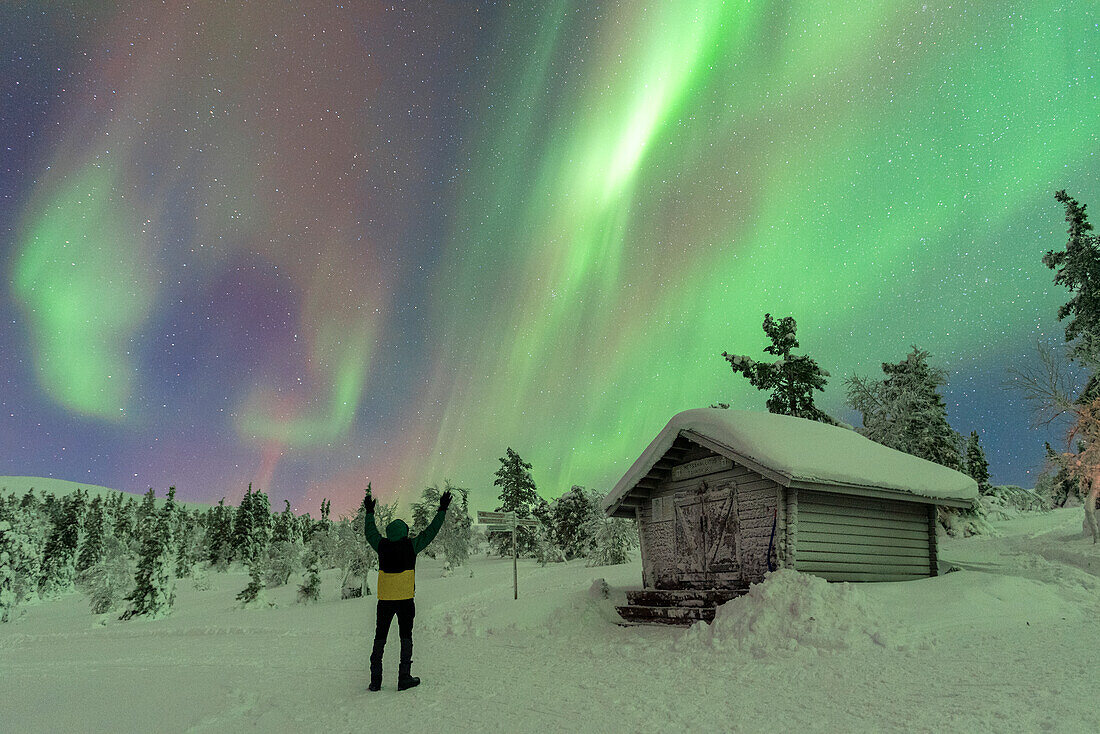 Happy tourist waving at the Northern Lights (Aurora Borealis) dancing in the night sky above the Arctic Circle, Akaslompolo, Kolari municipality, Finland, Europe