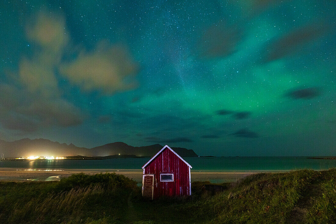 Nordlicht (Aurora Borealis) füllt den Himmel über der roten Hütte in der Nähe von Ramberg Strand während einer Herbstnacht, Lofoten Inseln, Nordland, Norwegen, Skandinavien, Europa