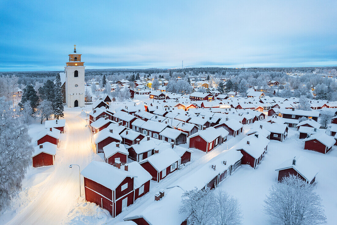 Winterliche Luftaufnahme des alten, schneebedeckten, beleuchteten Gammelstad mit roten Häusern um die Kirche, Gammelstad Kirchenstadt, UNESCO-Weltkulturerbe, Lulea, Norrbotten, Schwedisch-Lappland, Schweden, Skandinavien, Europa