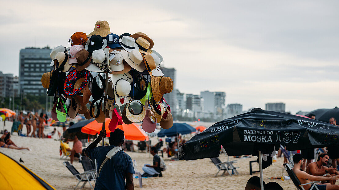 Verkäufer, der Hüte zum Verkauf anbietet, am Strand von Leblon in Rio de Janeiro, Brasilien, Südamerika