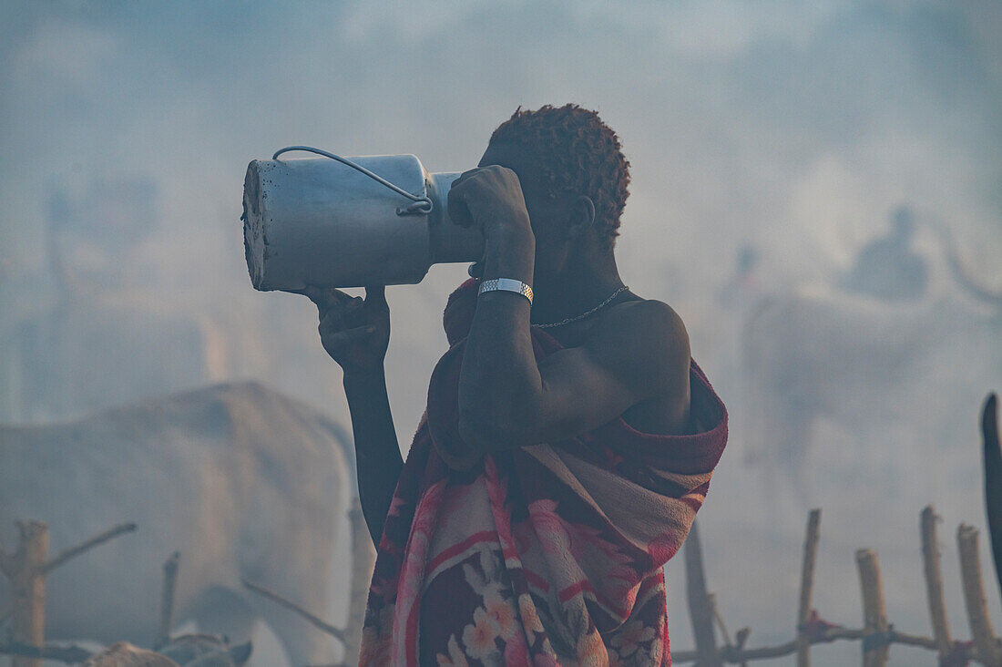 Gegenlichtaufnahme eines Mannes in einem Mundari-Viehlager beim Milchtrinken, Mundari-Stamm, Südsudan, Afrika