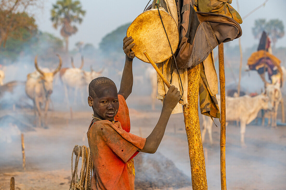 Mundari-Junge trommelt, um die Kühe zurückzurufen, Mundari-Stamm, Südsudan, Afrika