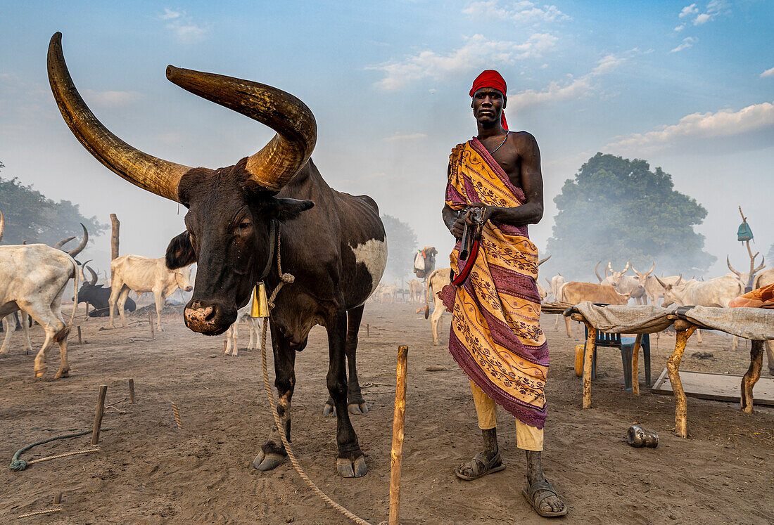 Mundari-Mann mit einer Kalaschnikow posiert mit einem Stier mit riesigen Hörnern, Mundari-Stamm, Südsudan, Afrika