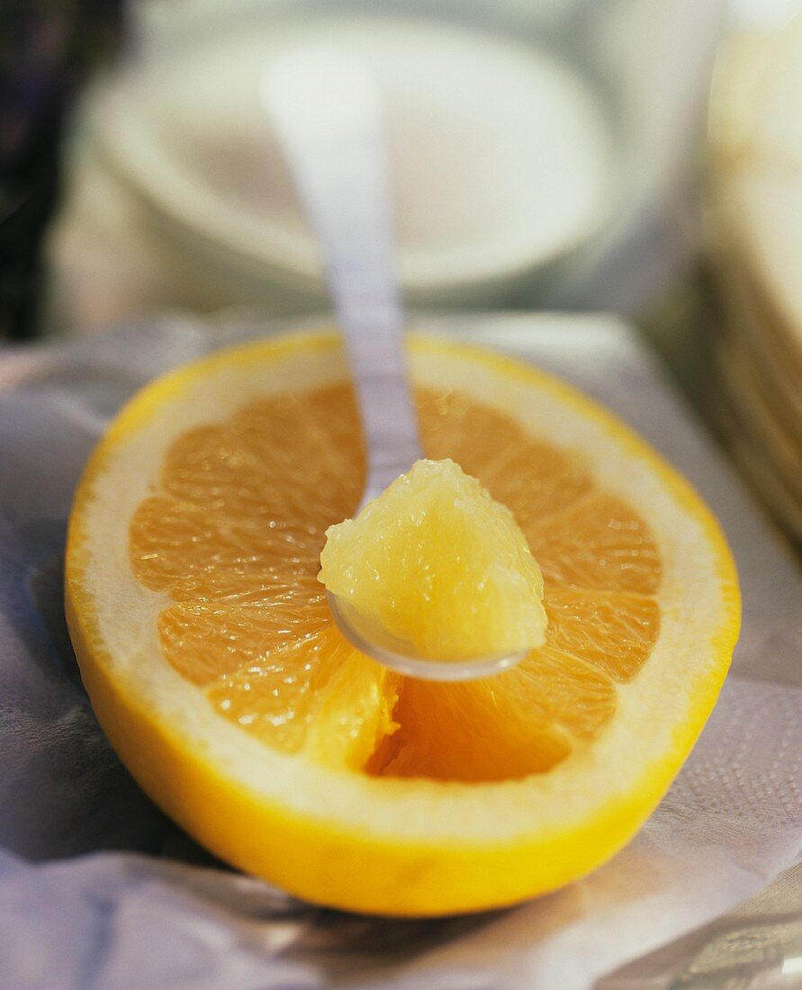 Grapfruitstück auf Löffel über gelber Grapefruithälfte