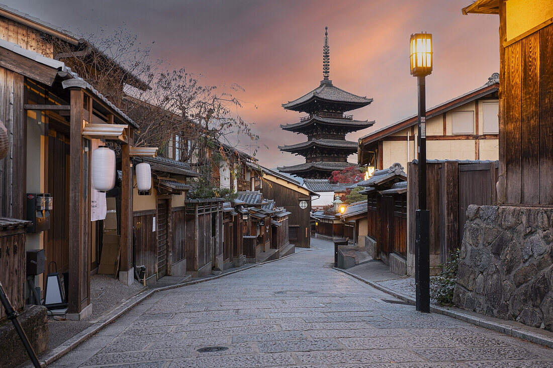 Eine schmale, von alten Gebäuden gesäumte Straße, die zur Hokan-ji-Gojunoto-Pagode führt, die sich in der Ferne gegen den Himmel bei Sonnenaufgang abzeichnet, Kyoto, Honshu, Japan, Asien