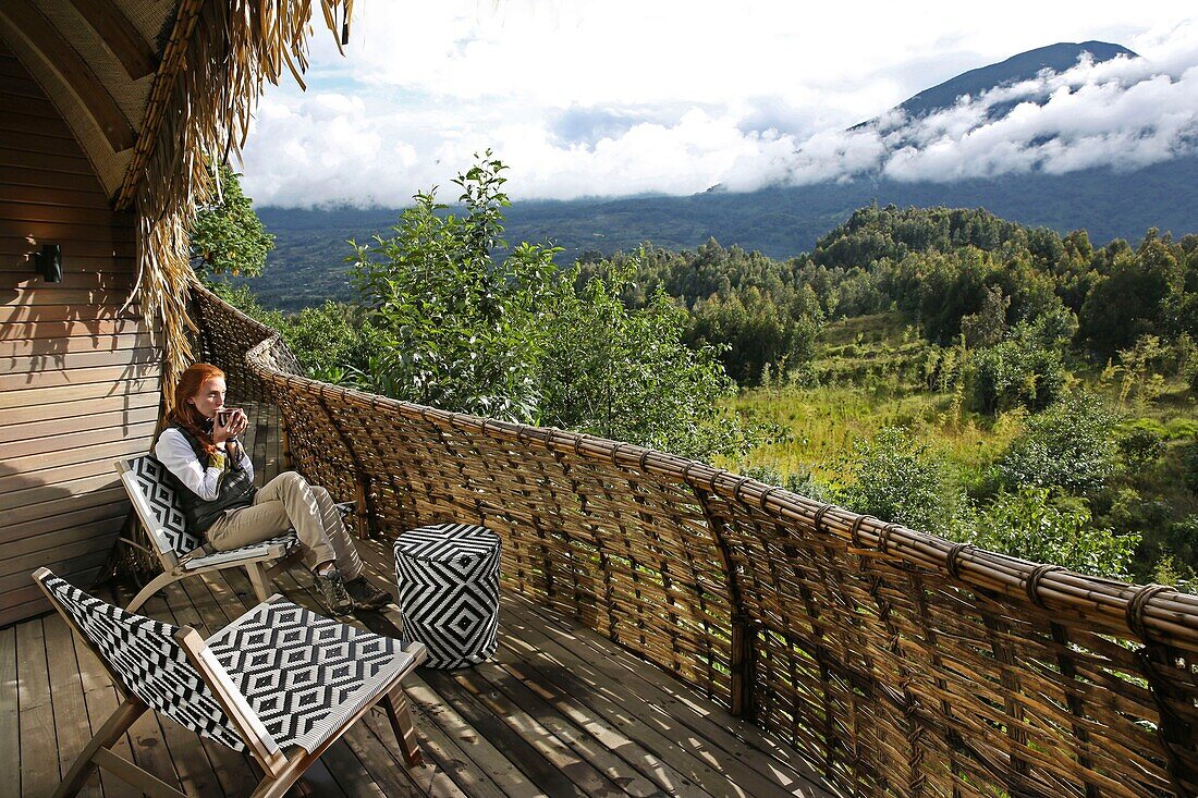 Ruanda, Volcanoes National Park, Frau beim Teetrinken auf der Terrasse einer Suite der Bisate Lodge, einer Lodge der Wilnderness Safaris Hotelgruppe, geöffnet am Mount Bisoke