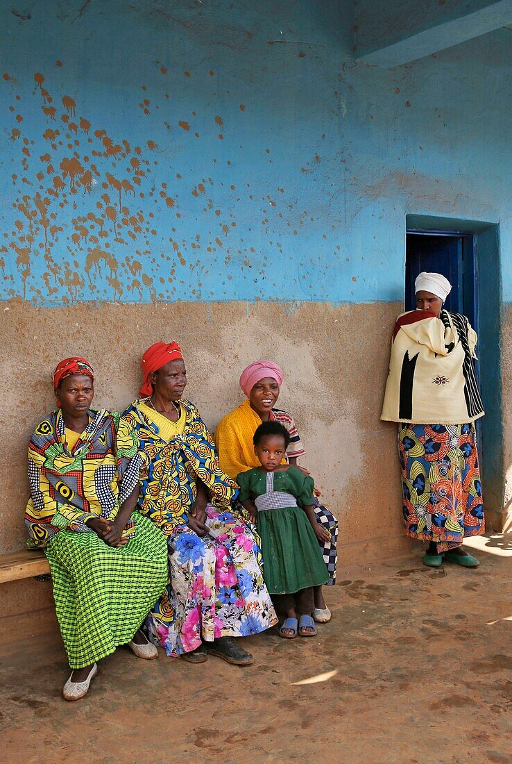 Ruanda, Zentrum des Landes, Dorfbewohner in buntem Lendenschurz sitzen auf einer Bank vor einer blauen Wand