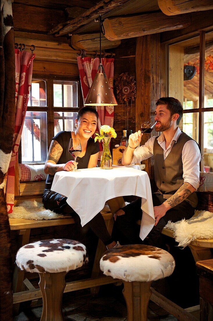 Italy, autonomous province of Bolzano, San Candido, young tattooed couple drinking a glass of wine in an alcove of the pizzeria helmhotel installed in the wooded setting of an old sheepfold