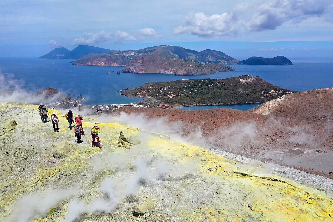 Italien, Sizilien, Äolische Inseln, Weltnaturerbe der UNESCO, Insel Vulcano, Wanderer am Kraterrand des Vulkans della Fossa durch Schwefelfumarolen, im Hintergrund die Insel Lipari und die Insel Salina (Luftaufnahme)