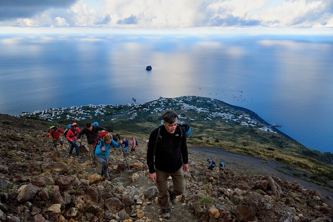 Italien, Sizilien, Äolische Inseln, von der UNESCO zum Weltnaturerbe erklärt, Insel Stromboli, Wanderer besteigen den Vulkan, im Hintergrund das Dorf Stromboli und die Insel Strombolicchio