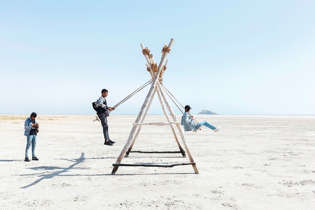 Marocco, Oued Ed-Dahab, Dakhla, Dakhla Attitude Resort, teens on swings on a beach at low tide