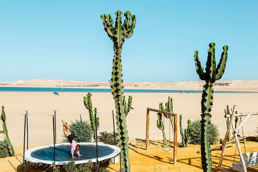 Marokko, Oued Ed-Dahab, Dakhla, Ocean Vagabond Resort, junges Mädchen spielt auf einem Trampolin am Meer in einem tropischen und wüstenartigen Klima