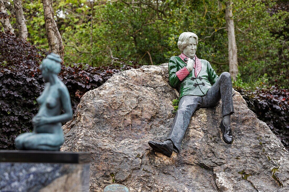 Irland, Dublin, Merrion Square, Denkmal zu Ehren des irischen Schriftstellers Oscar Wilde, der für sein ausschweifendes Leben bekannt war, Statuengruppe mit einer nackten Frau und einem lässig auf einem Felsen liegenden Schriftsteller in grüner und roter Anzugsjacke