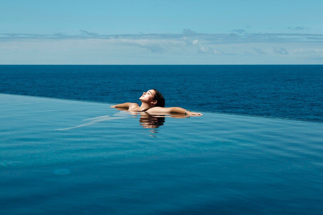 Spanien, Kanarische Inseln, La Palma, entspannte attraktive junge Frau beim Schwimmen im luxuriösen Infinity-Pool am Meer