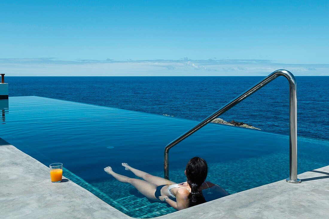 Spain, Canary Islands, La Palma, young seductive casual woman swimming in luxury infinity pool by the sea