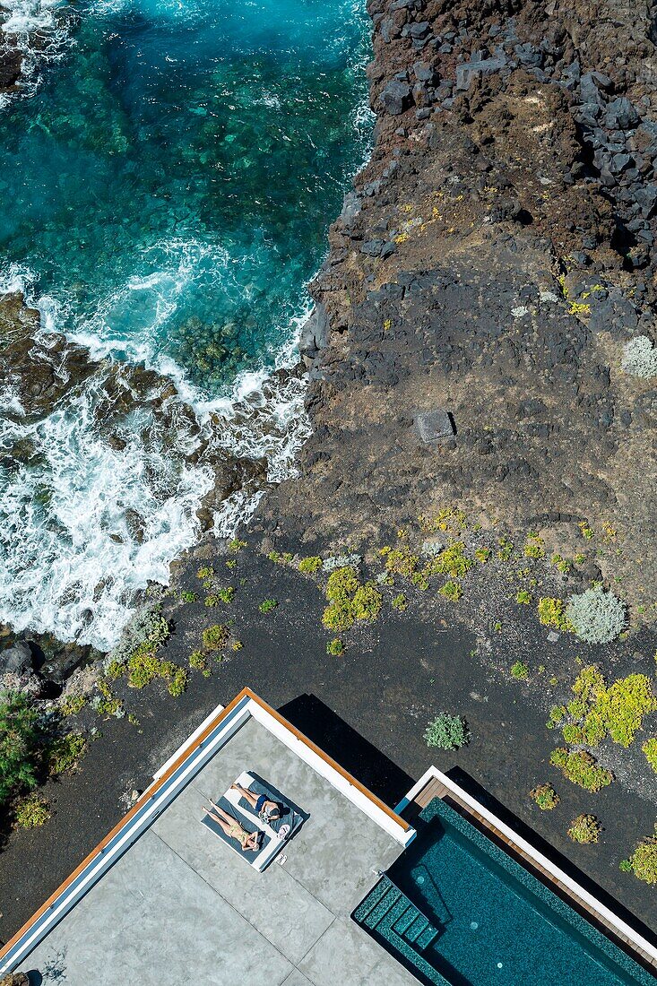 Spain, Canary Islands, La Palma, tourists resting at the edge of a swimming pool located by the sea (aerial view)