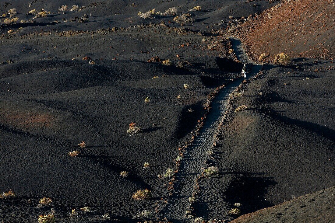 Spanien, Kanarische Inseln, La Palma, Wanderer auf einem Wanderweg in einer wüstenhaften und vulkanischen Umgebung bei Sonnenaufgang