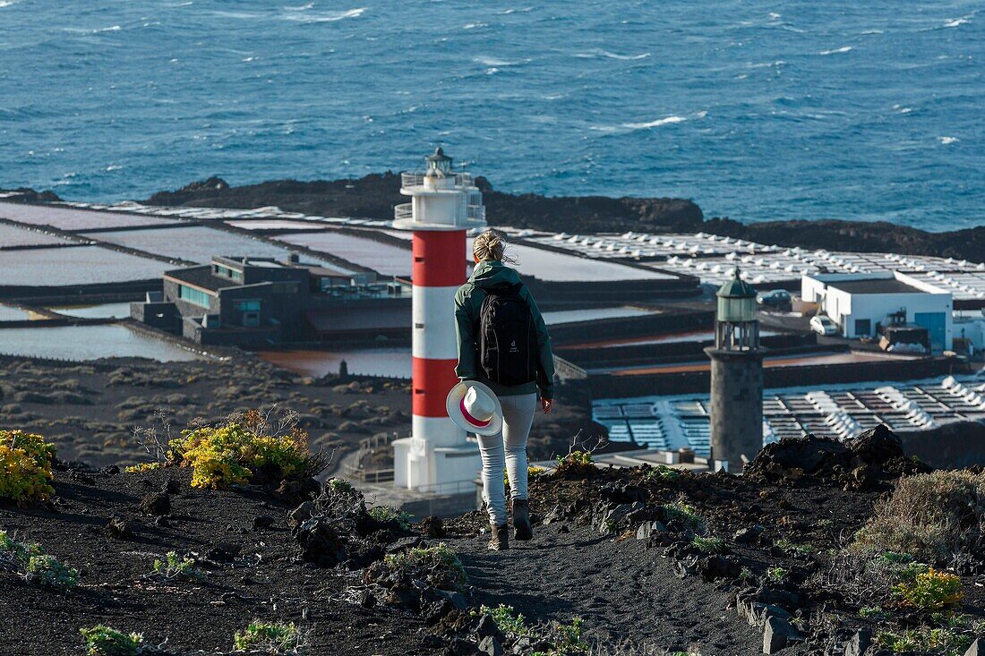 Spanien, Kanarische Inseln, La Palma, Wanderer auf einem Weg am Meer, in der Nähe eines Leuchtturms, umgeben von Salz