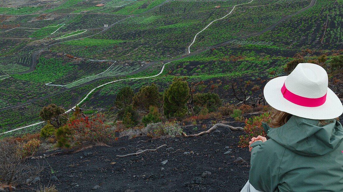 Spain, Canary Islands, La Palma, hiker sitting on the edge of the road, in front of a volcanic landscape