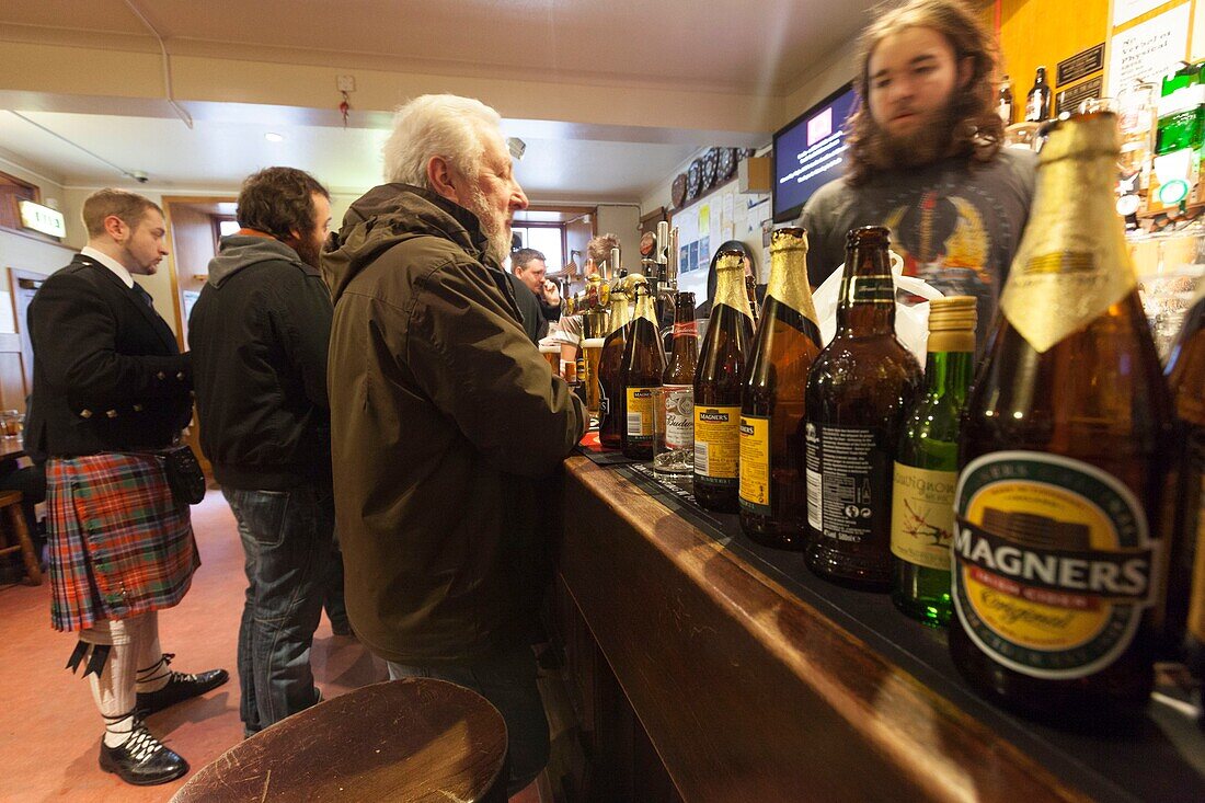 United Kingdom, Scotland, Shetland Islands, Mainland, Lerwick, man wearing a kilt in a pub and bottles of beer in the foreground