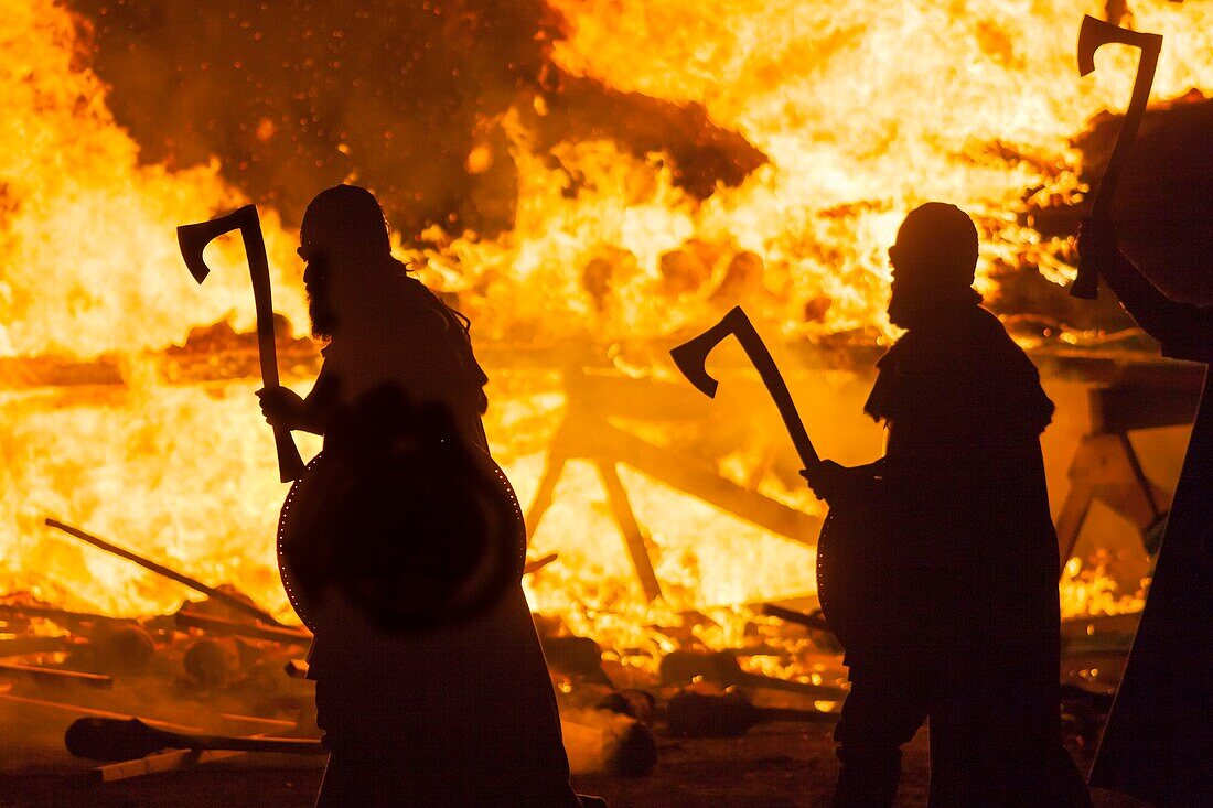 United Kingdom, Scotland, Shetland Islands, Mainland, Lerwick, Up Helly Aa festival, Guizers brandishing axes in front of the burning longship