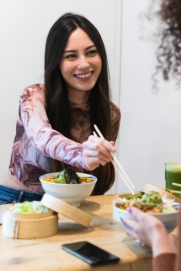 Female sitting at table eating with cropped anonymous friend eating tasty poke while spending weekend in restaurant