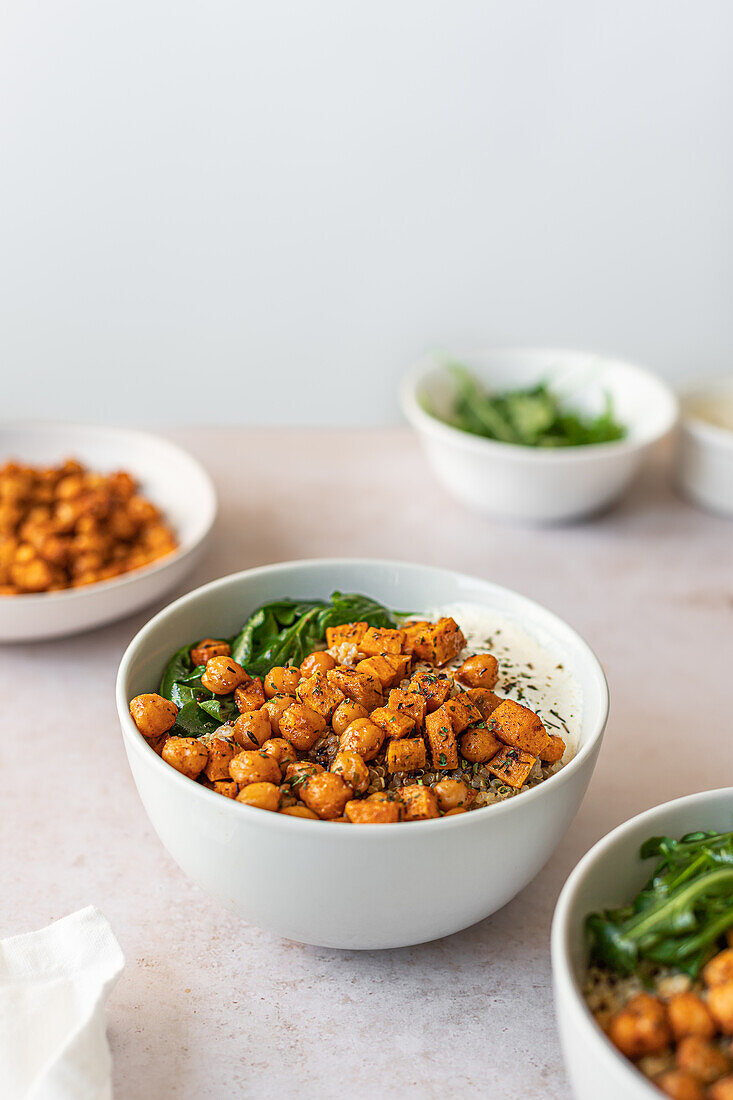 A nutritious quinoa salad bowl featuring spiced chickpeas, roasted sweet potatoes, fresh greens, and a creamy yogurt dressing