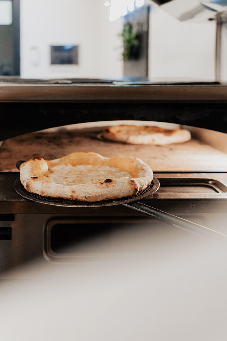 Pizzen werden in einem modernen Ofen in einer Pizzeria gebacken, die eine gemütliche Kücheneinrichtung in einem anonymen Anbau zeigt, der für eine vielseitige Verwendung gesichtslos ist