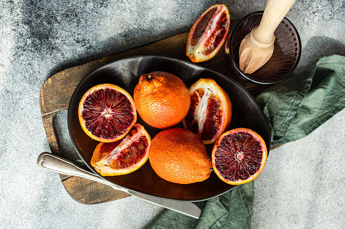 Halved blood oranges on a dark plate with a juicer, showcasing the vibrant red citrus