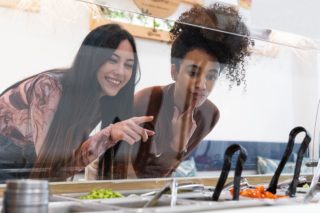 Multiracial female friends standing at counter and choosing food in restaurant while spending weekend together