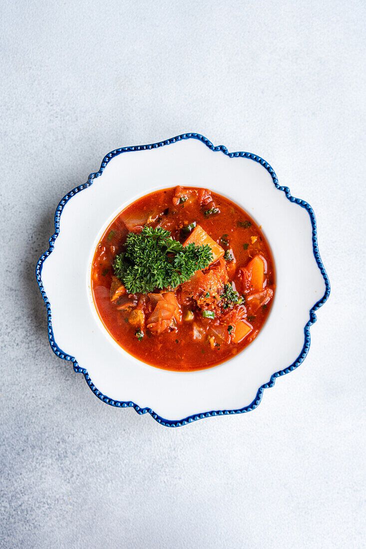 Dieses Bild zeigt eine herzhafte Portion traditionellen ukrainischen Borschtsch, eine Rote-Bete-Suppe mit Fleischstückchen und einem Klecks saurer Sahne, garniert mit Petersilie