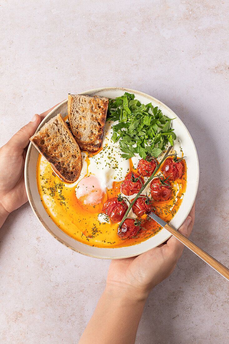 A savory plate of Turkish eggs perched on creamy Greek yogurt, drizzled with spiced butter and garnished with tomatoes and parsley, served with toast