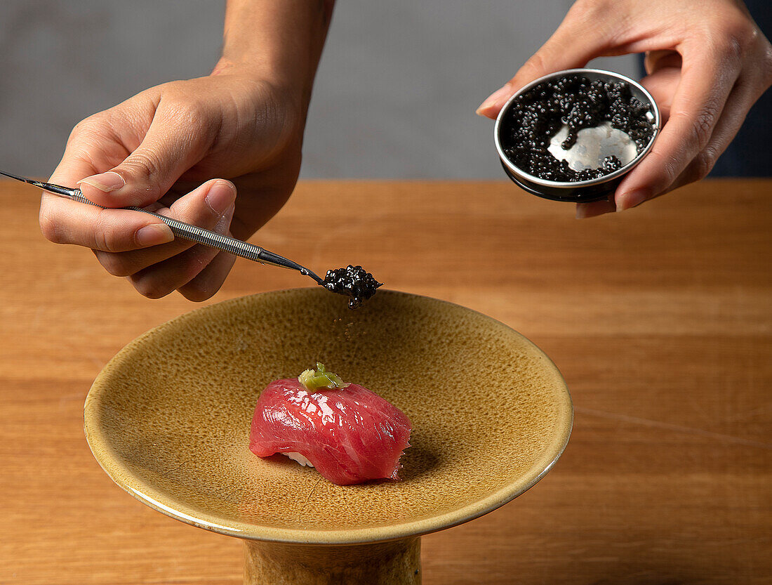 A chef's precise hand garnishes a sushi piece with caviar from a small dish, demonstrating meticulous culinary skill and sushi art