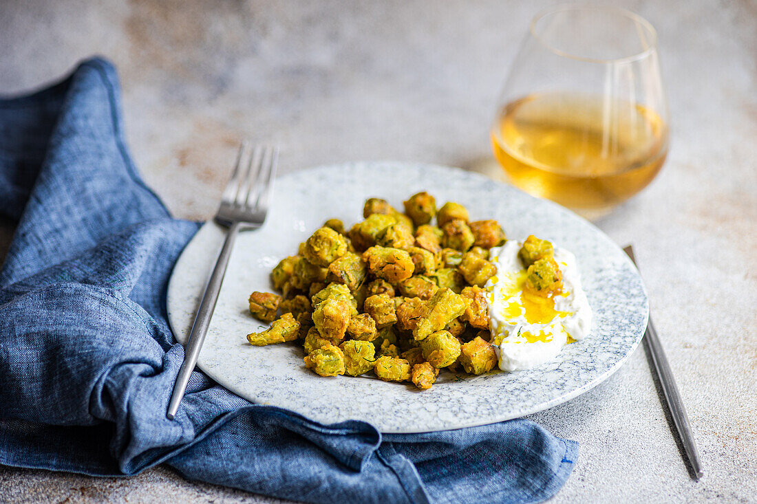 Gebratene Bamia, serviert auf einem Keramikteller mit einem Klecks Sauerrahmsoße, gemischt mit Dill und Knoblauch Ideal für die mediterrane Küche Ein Glas Weißwein ergänzt das Arrangement