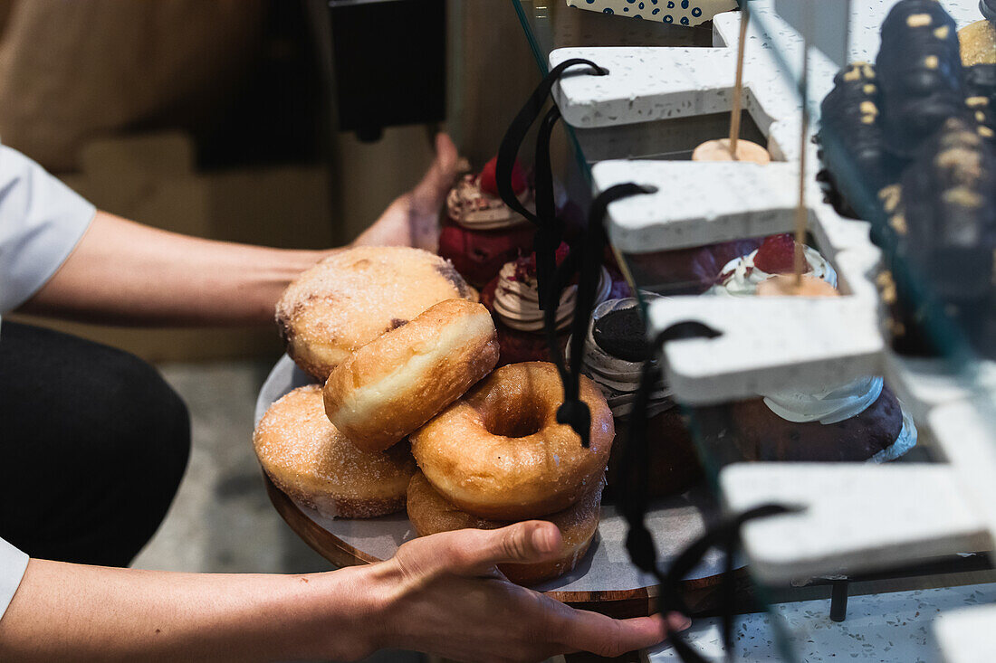 High angle of crop anonymous baker putting vegan donuts on tray on showcase in bakery