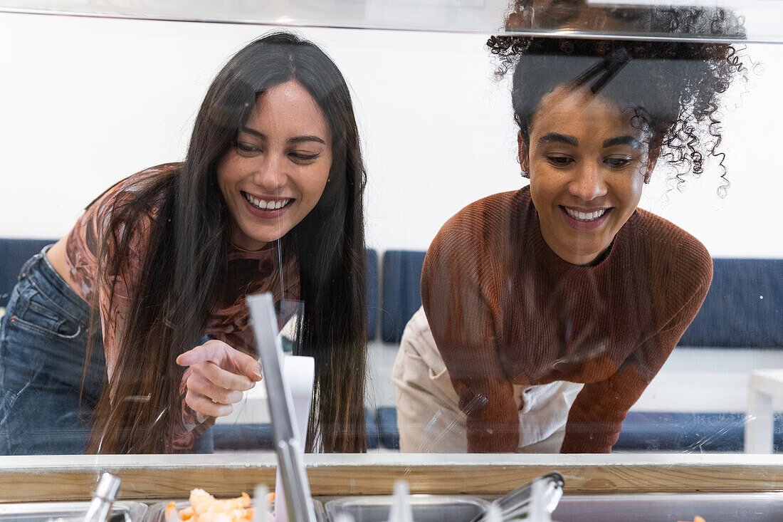 Multiracial female friends standing at counter and choosing food in restaurant while spending weekend together