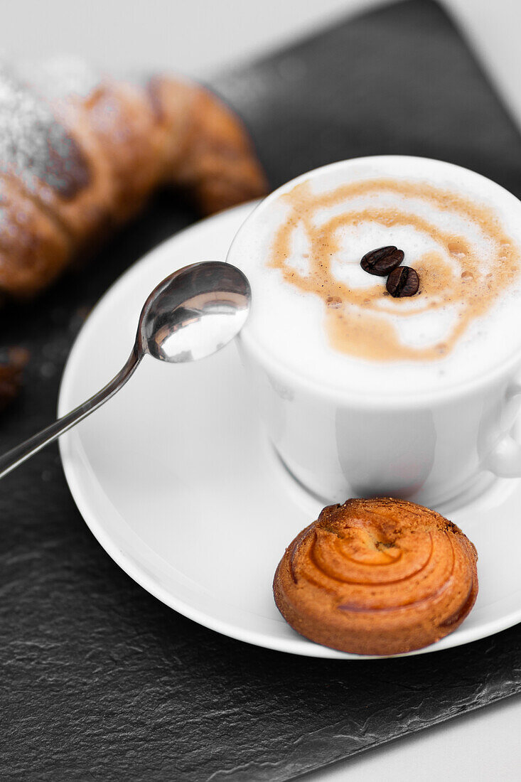 Eine frisch gebrühte Tasse kolumbianischen Kaffees, begleitet von einem butterweichen, hausgemachten Croissant, das elegant auf einem Schiefertablett serviert wird.