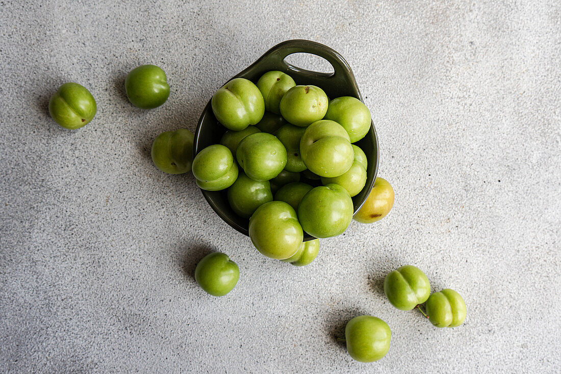 Overhead view of ripe organic green plums in a dark bowl, commonly used in cuisines across the Mediterranean region