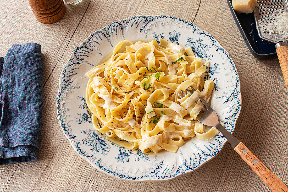 From above, Homemade Italian pasta garnished with fresh parsley and grated Parmesan on a wooden table with pepper mill and cheese grater