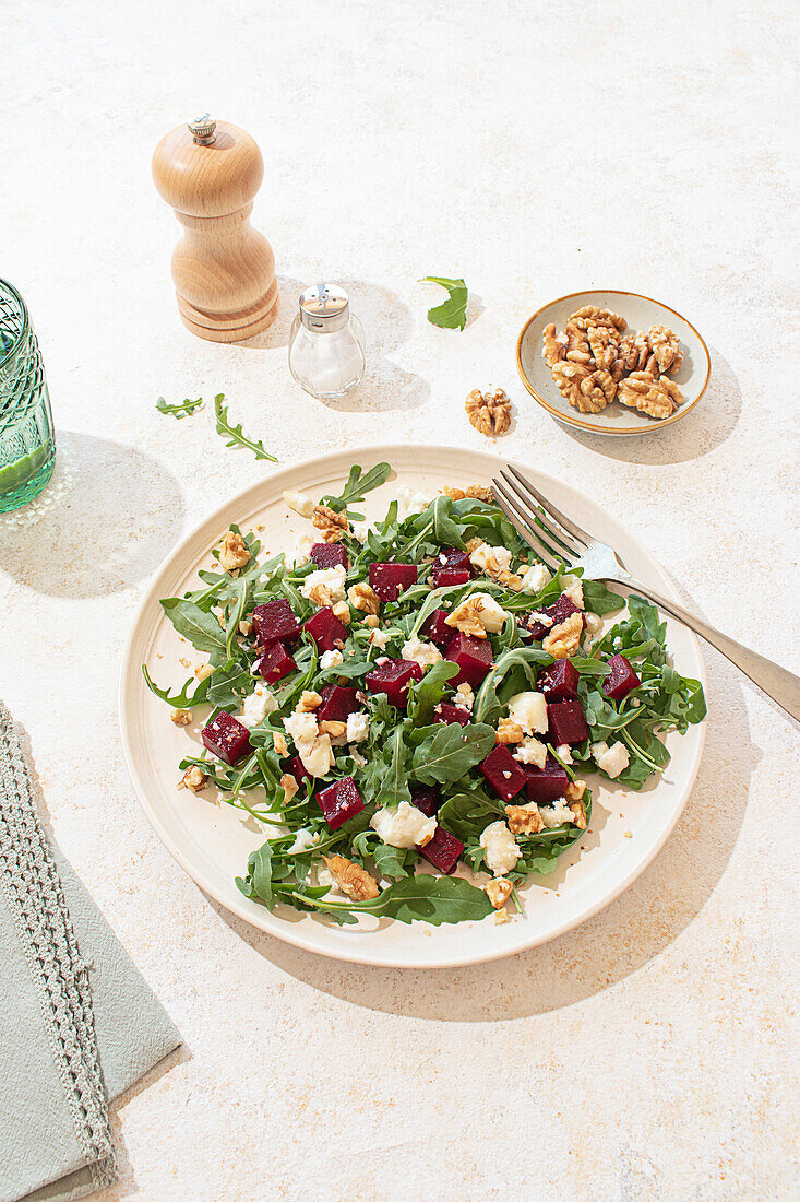 A beautifully styled arugula salad with goat cheese, walnuts, and beetroot on a light beige plate. Natural light highlights the vibrant colors and textures, creating a fresh and inviting atmosphere