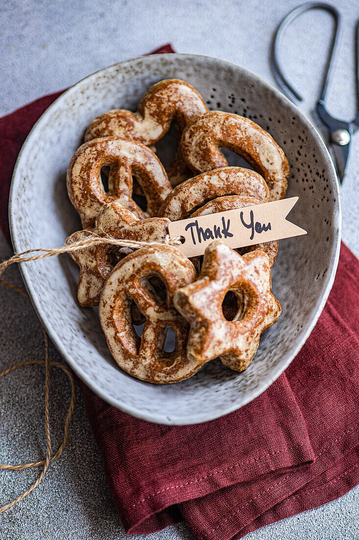 Top view of homemade star-shaped gingerbread cookies, dusted with sugar and presented in a speckled ceramic bowl, accompanied by a Thank You tag, all set on a red napkin.