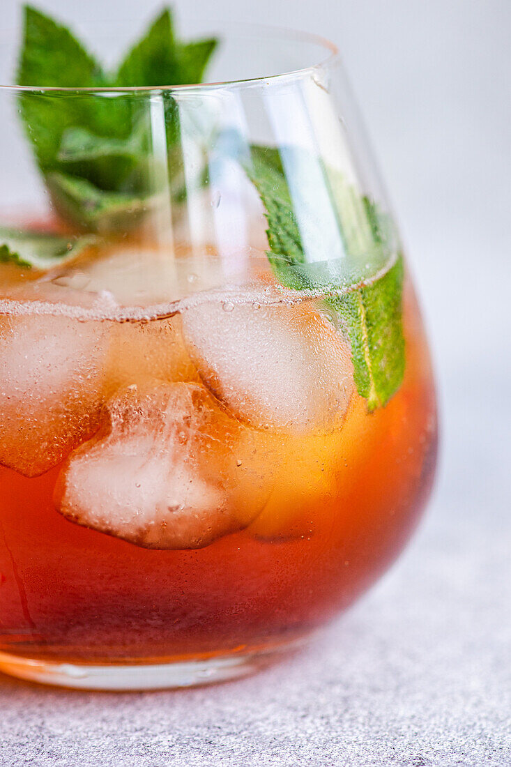 Close-up of a chilled Coke cocktail, beautifully garnished with fresh mint leaves in a clear glass. Ice cubes and a subtle fizz enhance the drink's appeal, set against a soft, textured background.