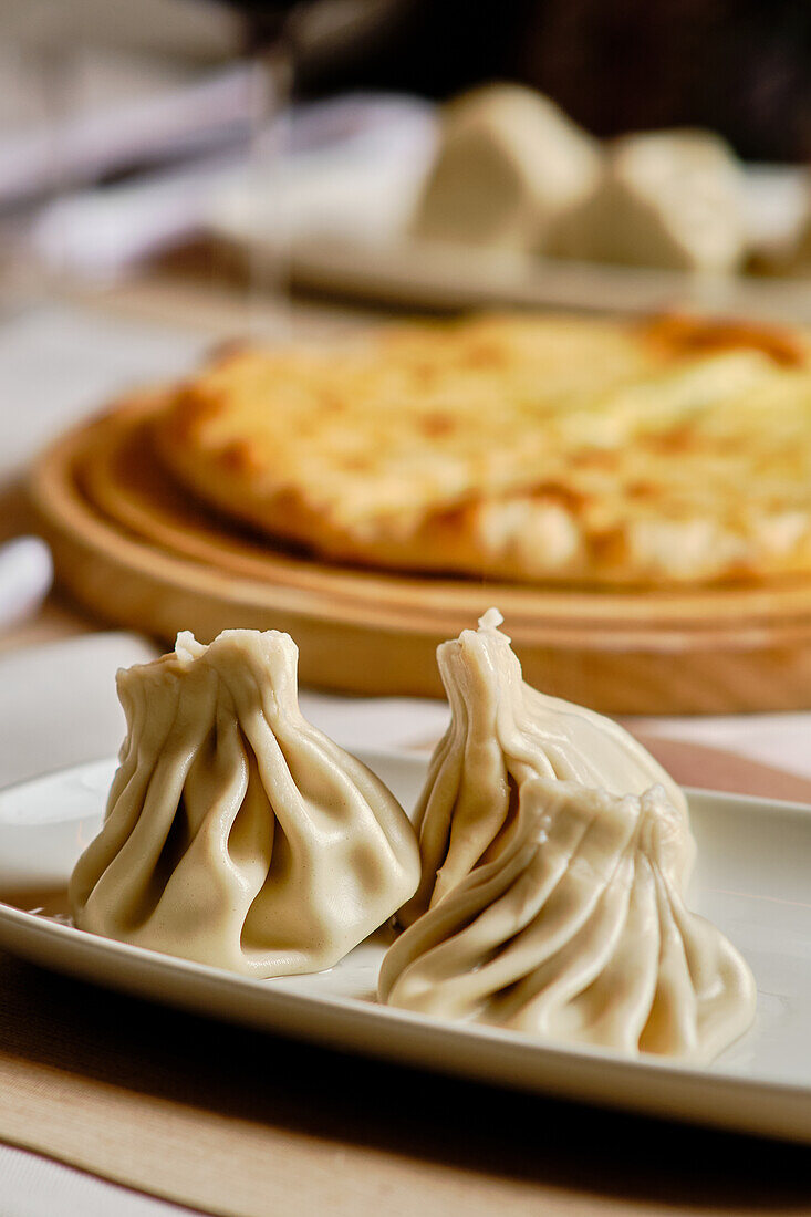 A delicious selection of Georgian cuisine, featuring khinkali dumplings on a ceramic plate and khachapuri cheese bread on a wooden serving board in the background